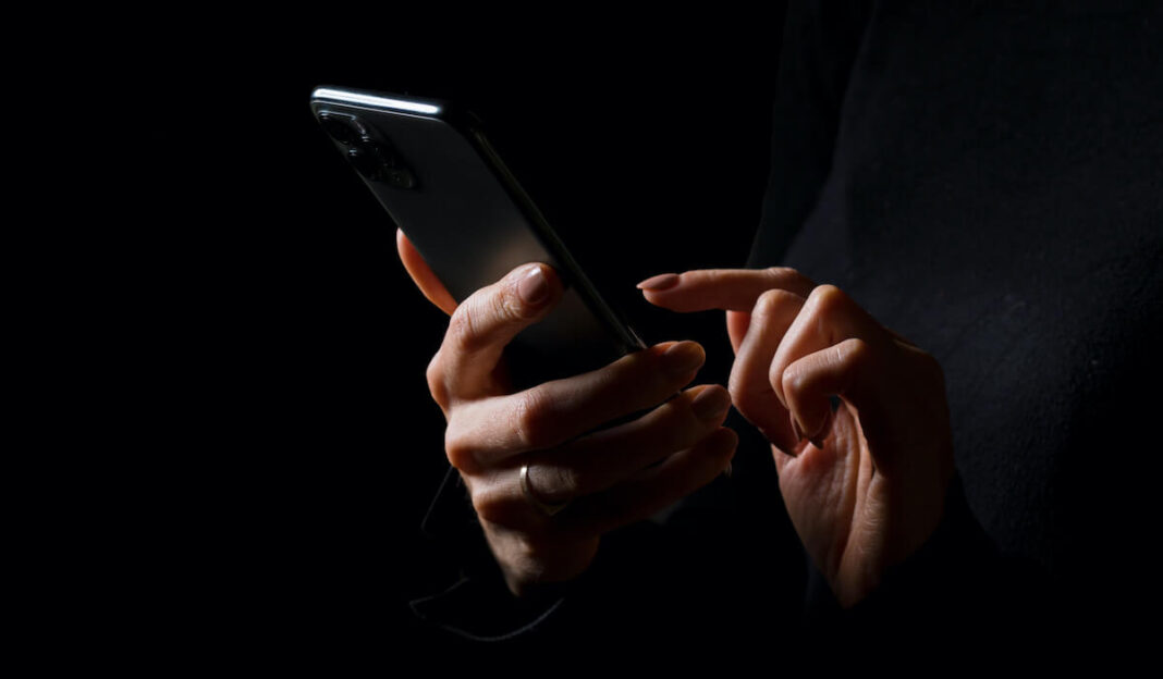 A dark backgrounded picture showing two hands holding a mobile phone.