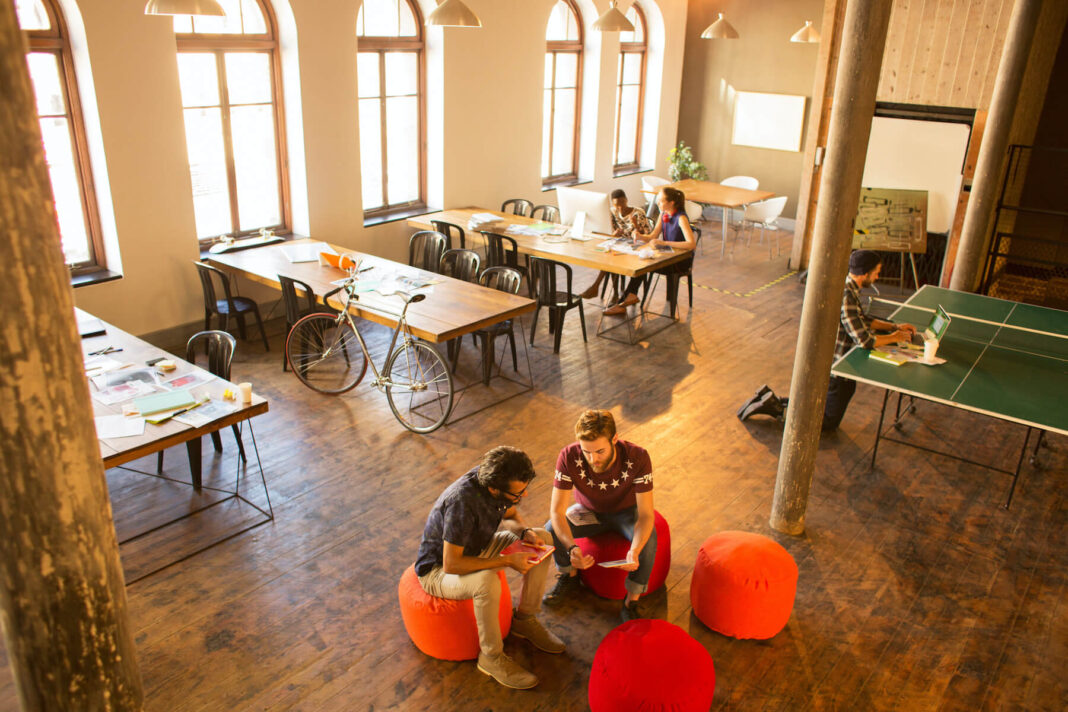 A white study room with tables and a table tennis table in it, few people talking.