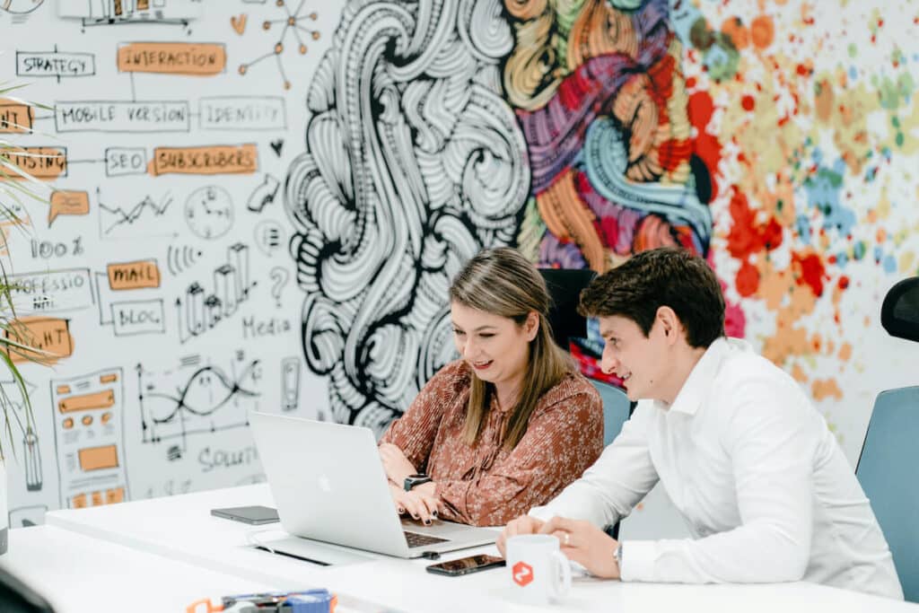 Two Zenitech employees sat in front of colourful art wall looking at laptop