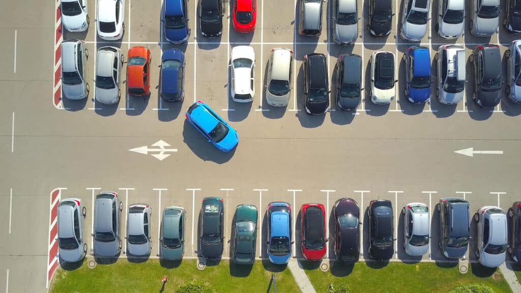Aerial view of an outside car park with a blue car trying to park in a space