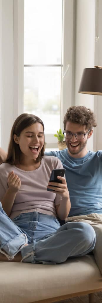 A couple sat on a sofa cheering at something on their phone