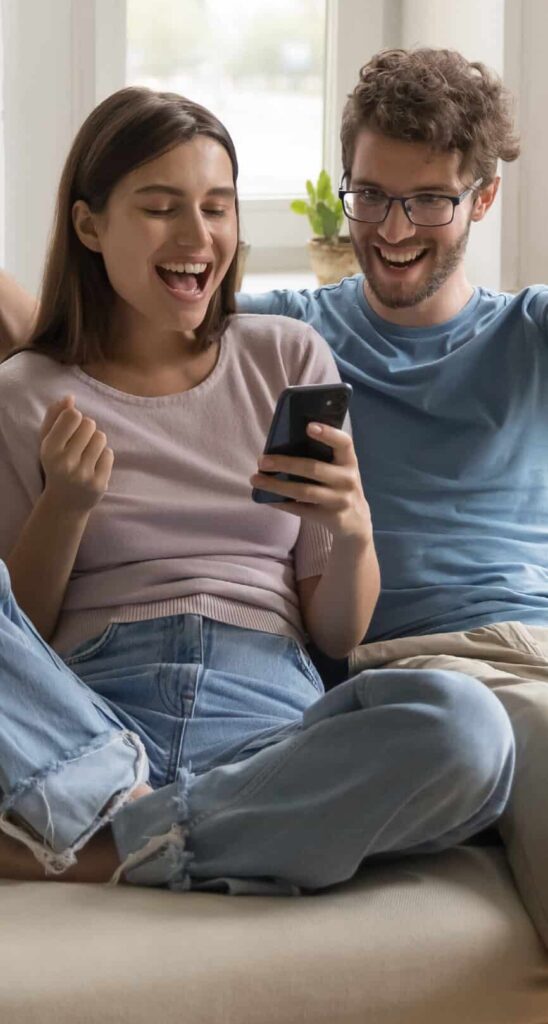 A couple sat on a sofa cheering at something on their phone