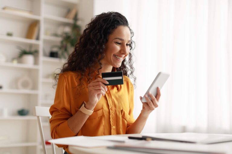 Woman sat at desk holding bank card and mobile phone
