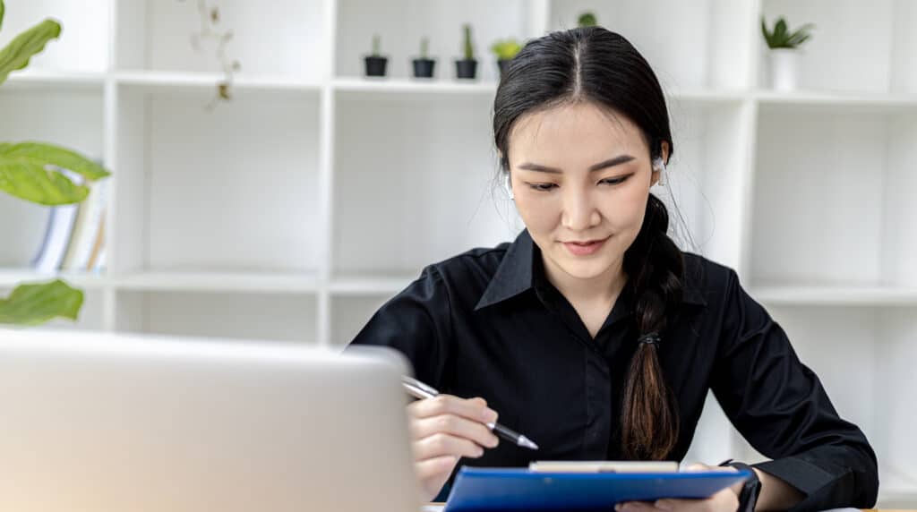 Woman in black shirt sat at table holding a pen and pad of paper