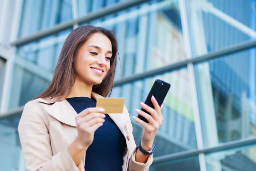 Woman stood in front of office building holding a bank card and mobile phone