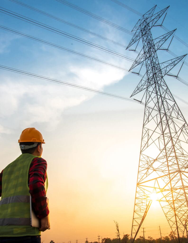 Man in hard hat and high vis vest stood looking up at an electricitiy pylon