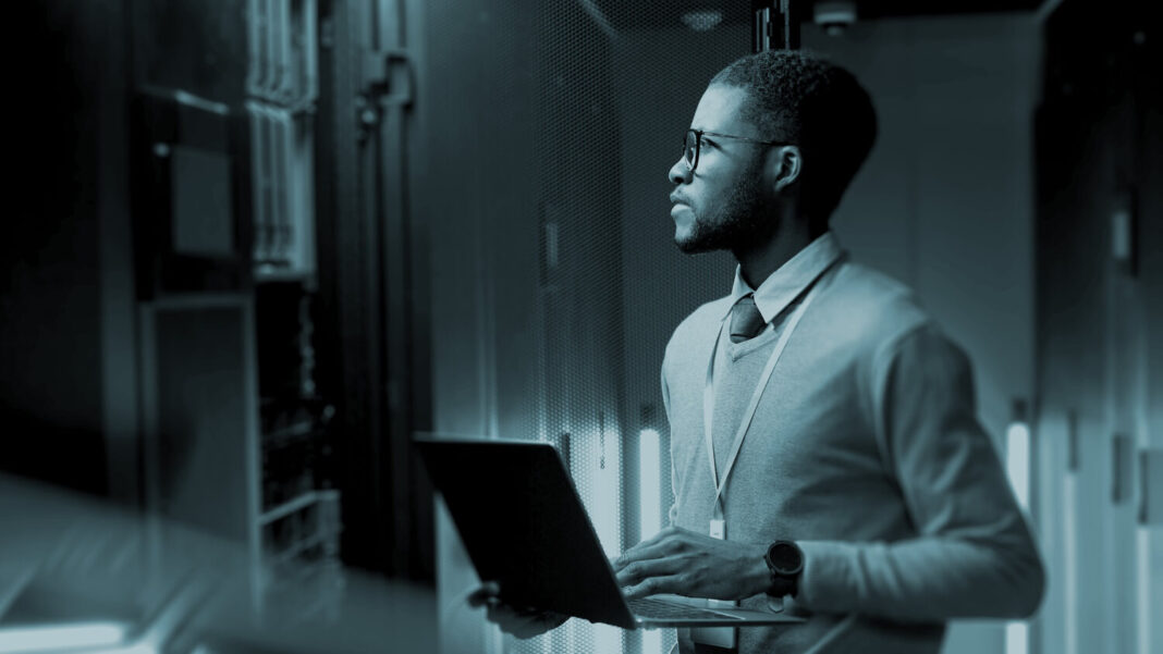 IT professional in a server room, holding a laptop and examining server racks, representing strategic planning for cloud infrastructure.